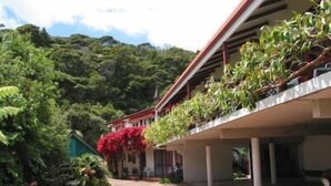Un bâtiment doté d’une galerie couverte, entouré d’une végétation luxuriante et avec une chaîne de montagnes en toile de fond.