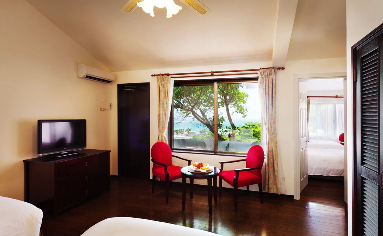 A hotel room with a TV, a dining table with chairs, a window with a view, and a bed.