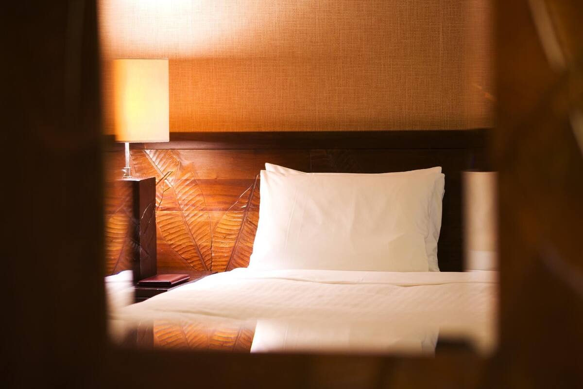 A hotel room with a bed, a nightstand, and a lamp.