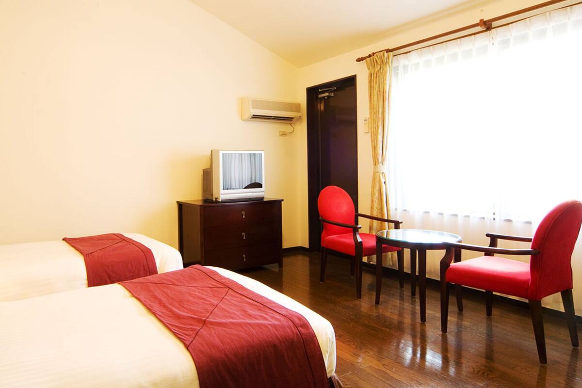 A hotel room with two beds, a desk with a lamp, a television, a chair, and a table.