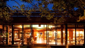 A modern building with large glass doors, a wooden deck, and indoor seating areas. - Coco Garden Resort Okinawa (Uruma)