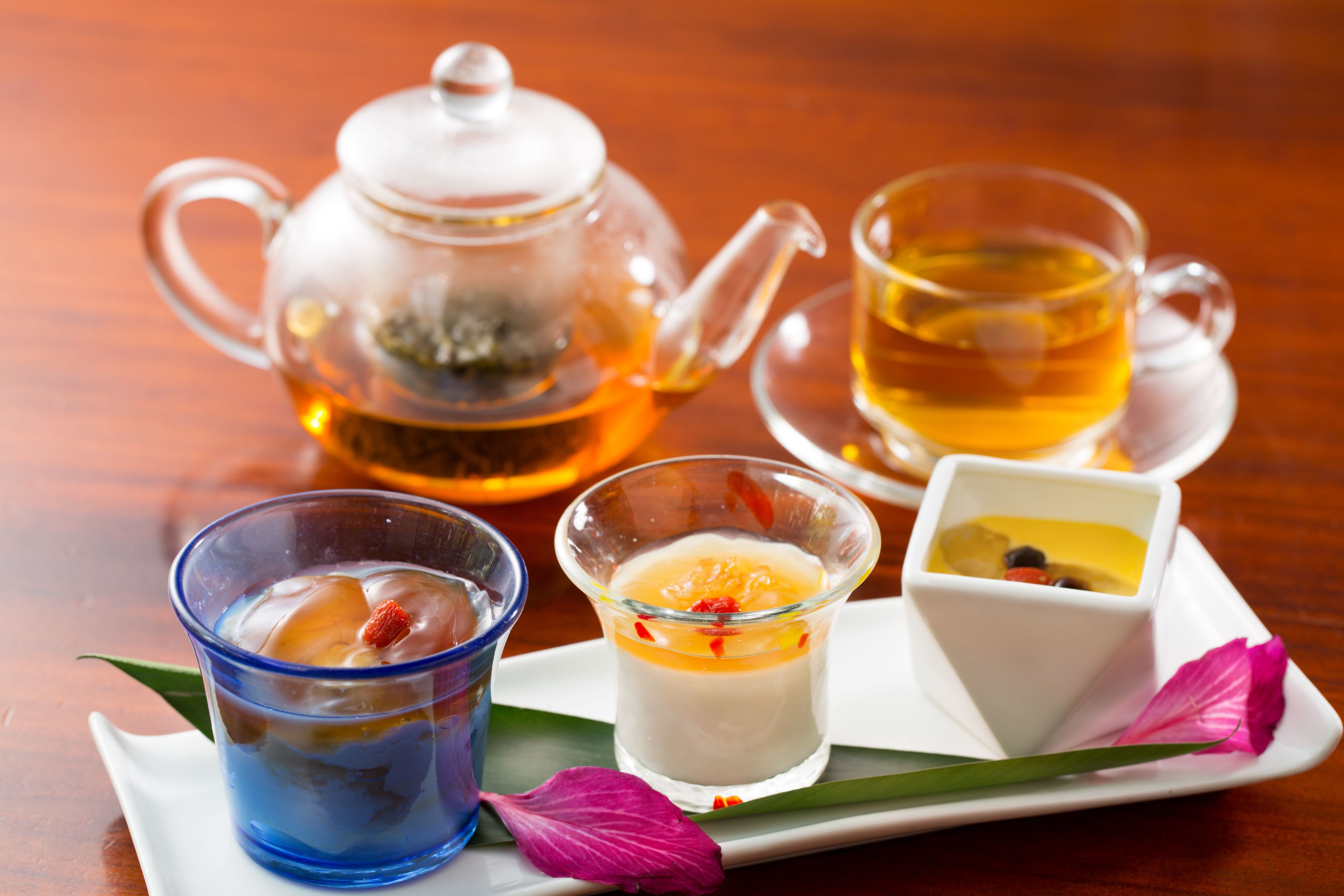 Una mesa con una tetera de vidrio, dos tazas de té y dos platos pequeños para postre.
