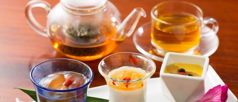Una mesa con una tetera de vidrio, dos tazas de té y dos platos pequeños para postre.