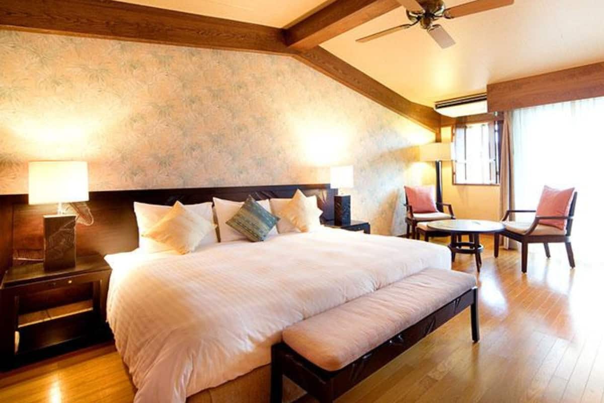 A bedroom with a large bed, bedside tables, a ceiling fan, and a seating area with a table and chairs.
