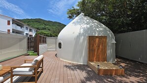 Una estructura en forma de cúpula con una puerta de madera, una pequeña plataforma de madera y una zona de estar con cojines.