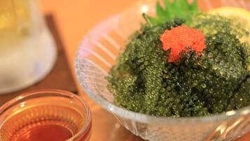 A bowl of green caviar with a red topping, a small glass of red liquid, and a blurred background.