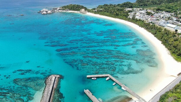 Vista aérea de una zona costera con aguas turquesas cristalinas, una playa de arena y un pequeño muelle.
