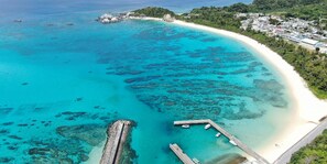 Vista aérea de una zona costera con aguas turquesas cristalinas, una playa de arena y un pequeño muelle.