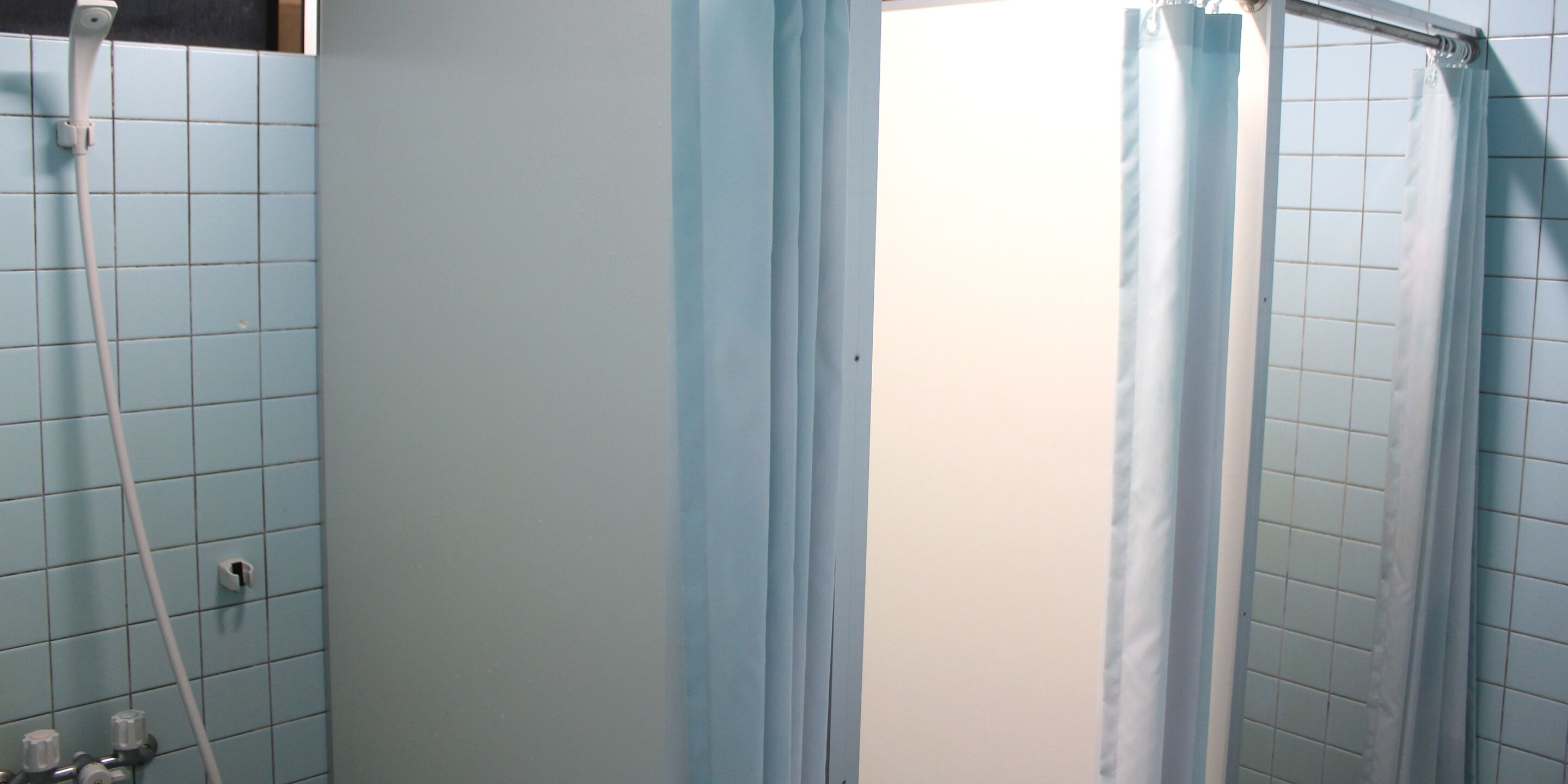 A bathroom with light blue tiles, a shower curtain, and a visible shower hose.