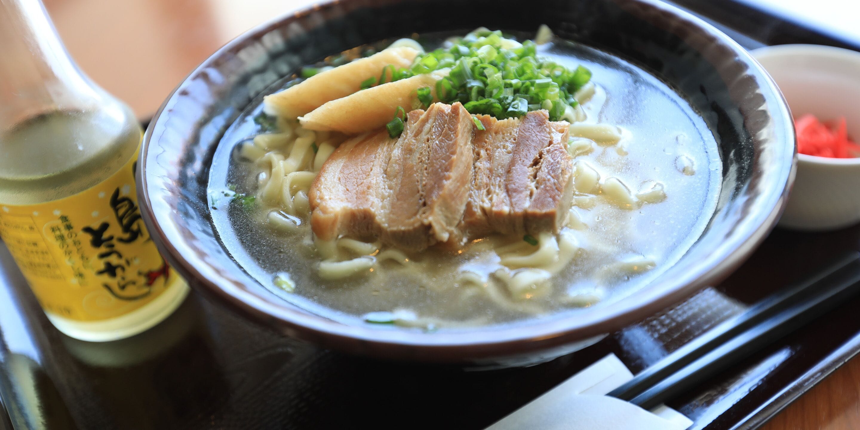 A bowl of ramen with noodles, pork, and green onions.