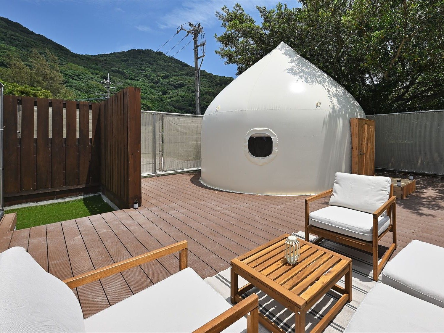 Una estructura de domo geodésico con una pequeña ventana circular, rodeada por una terraza de madera con mobiliario exterior.