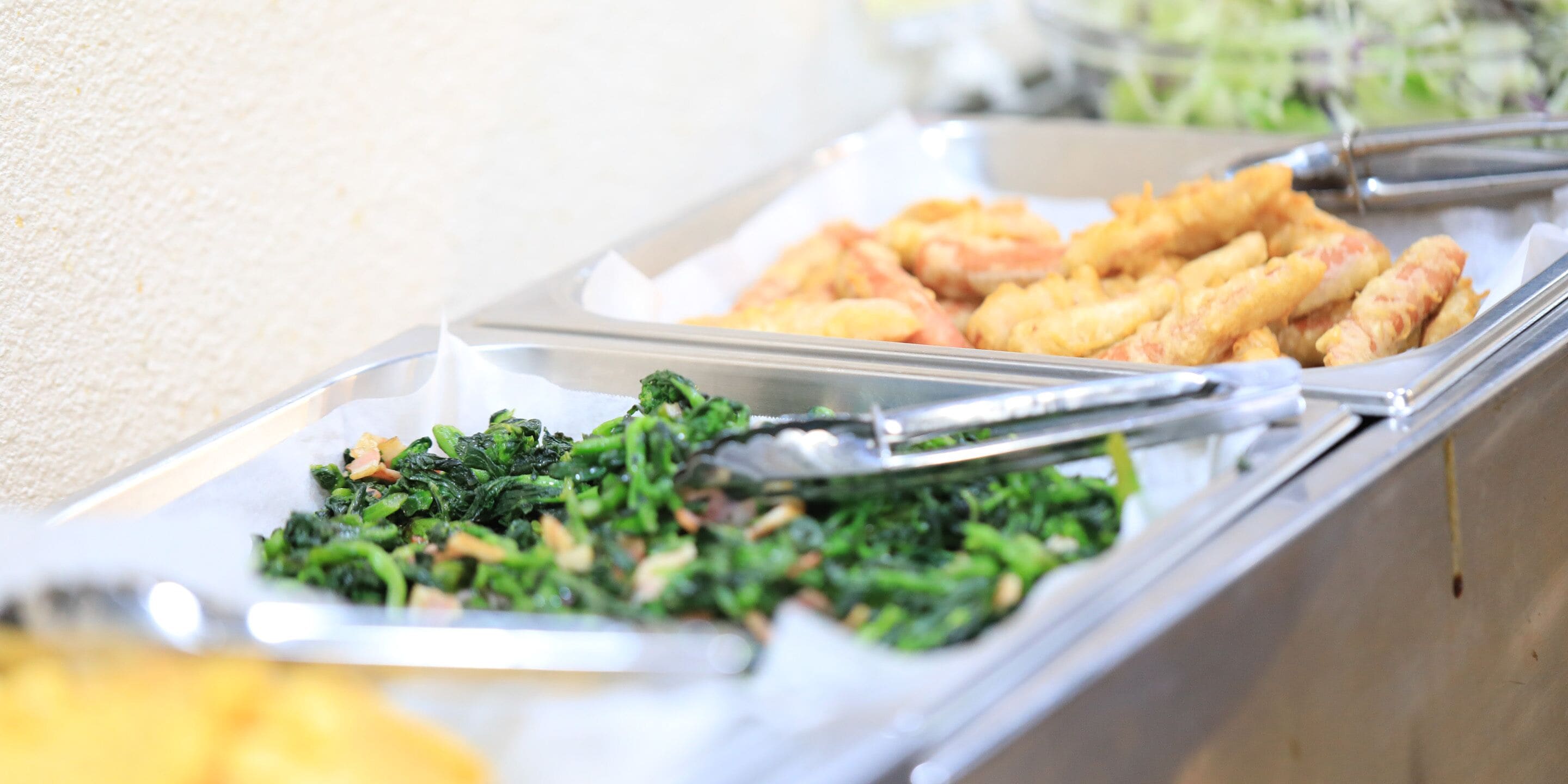 A buffet with trays of food including greens and fried items.