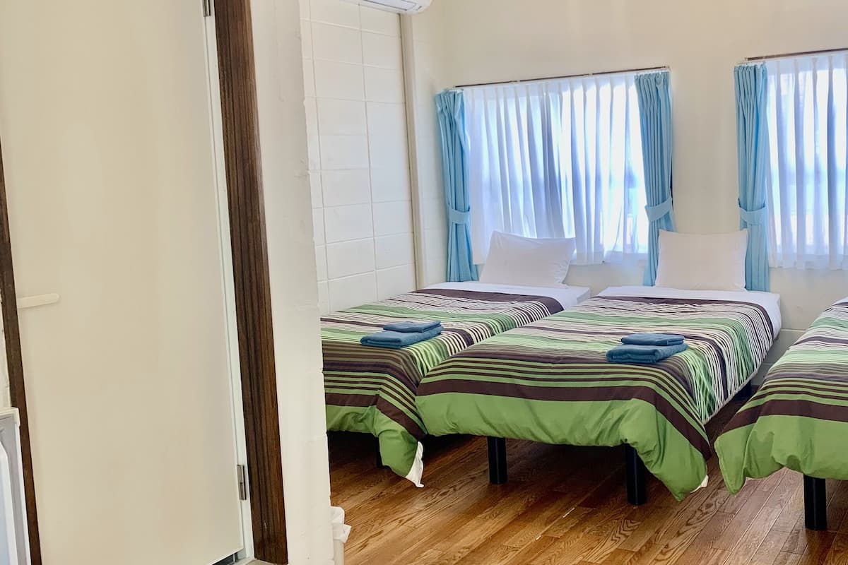 Una habitación con dos camas, cada una con ropa de cama y toallas a rayas, suelo de madera y cortinas en las ventanas.