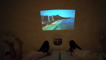 Une projection représentant une scène de plage sur un mur, deux lits avec des oreillers et une petite fenêtre.