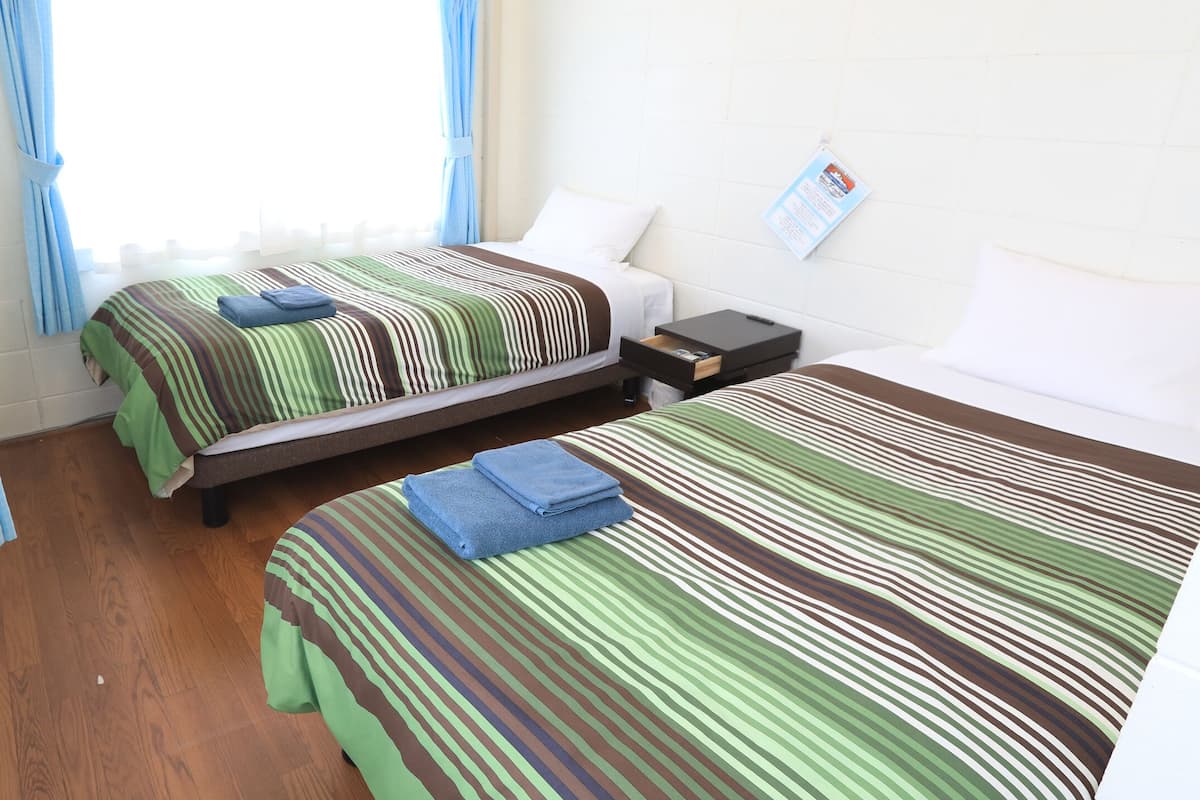 Habitación de hotel con dos camas, piso de madera y ventana con cortinas.