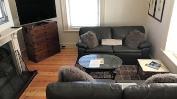 A living room with a black leather sofa, a glass coffee table, a fireplace, and a television.