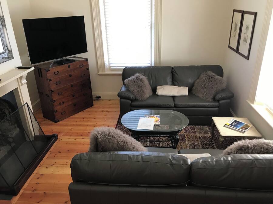 A living room with a black leather sofa, a glass coffee table, a fireplace, and a television.