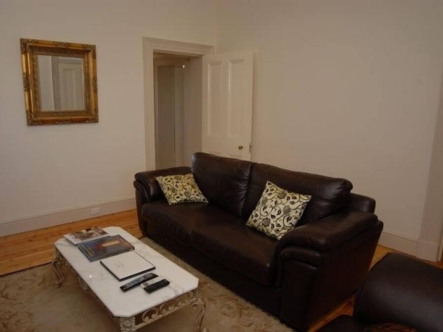 A living room with a brown leather sofa, a white coffee table, and a mirror on the wall.