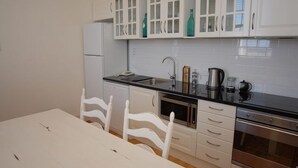 Une cuisine compacte avec des meubles blancs, un plan de travail noir, un four en acier inoxydable et une table à manger blanche avec des chaises.