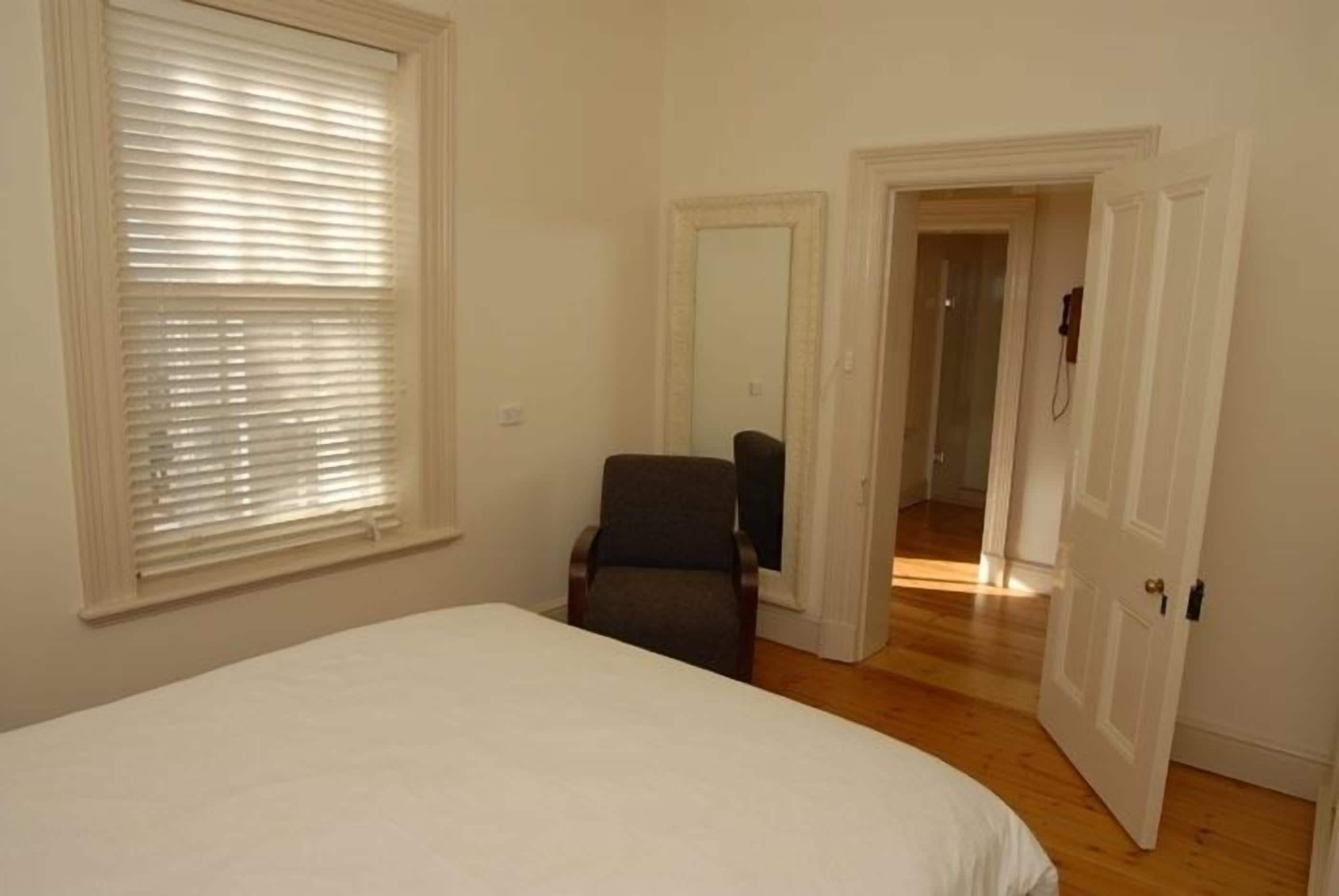 Quarto com cama, cadeira, espelho e porta que dá para outro cômodo.