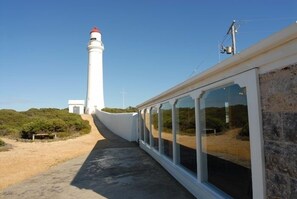 A pathway leading to a lighthouse with a red top, surrounded by greenery and a clear sky.