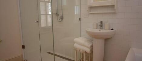 A modern bathroom with a glass-enclosed shower, a pedestal sink, and a white tiled wall.