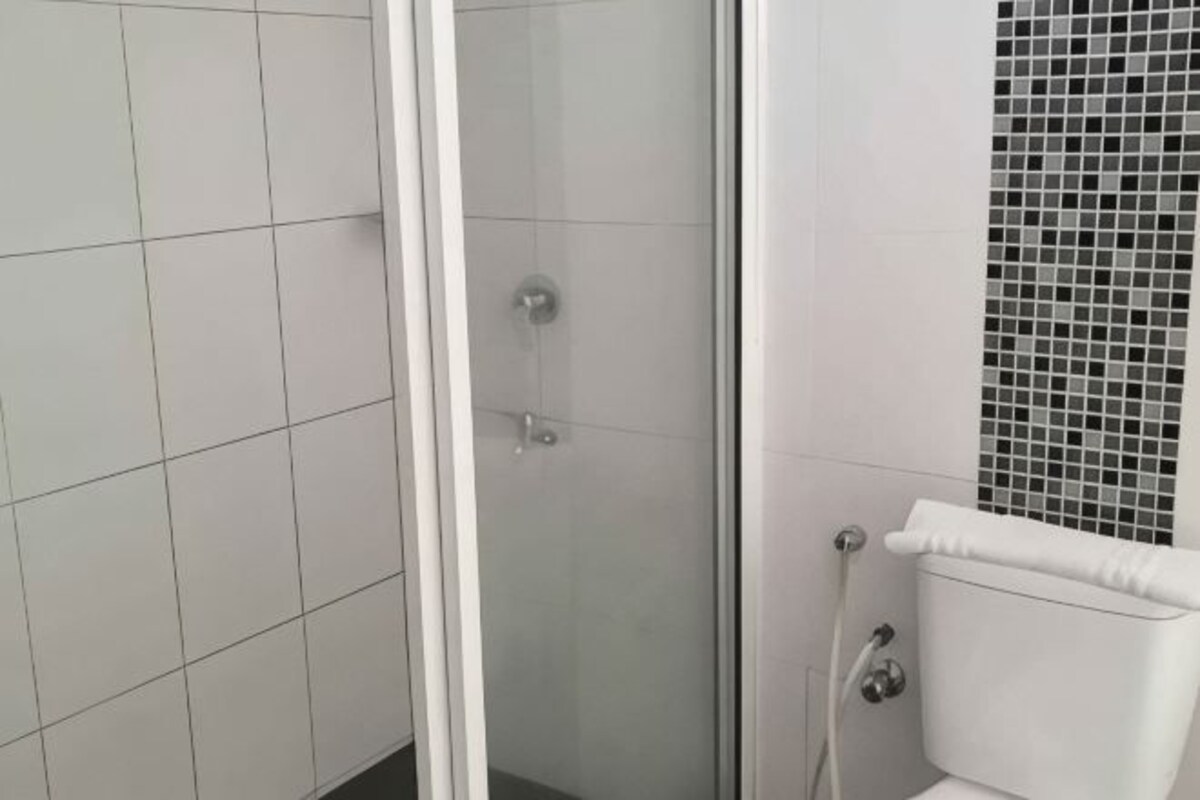 A bathroom with white tiled walls, a glass shower enclosure, and a mosaic tile accent wall.