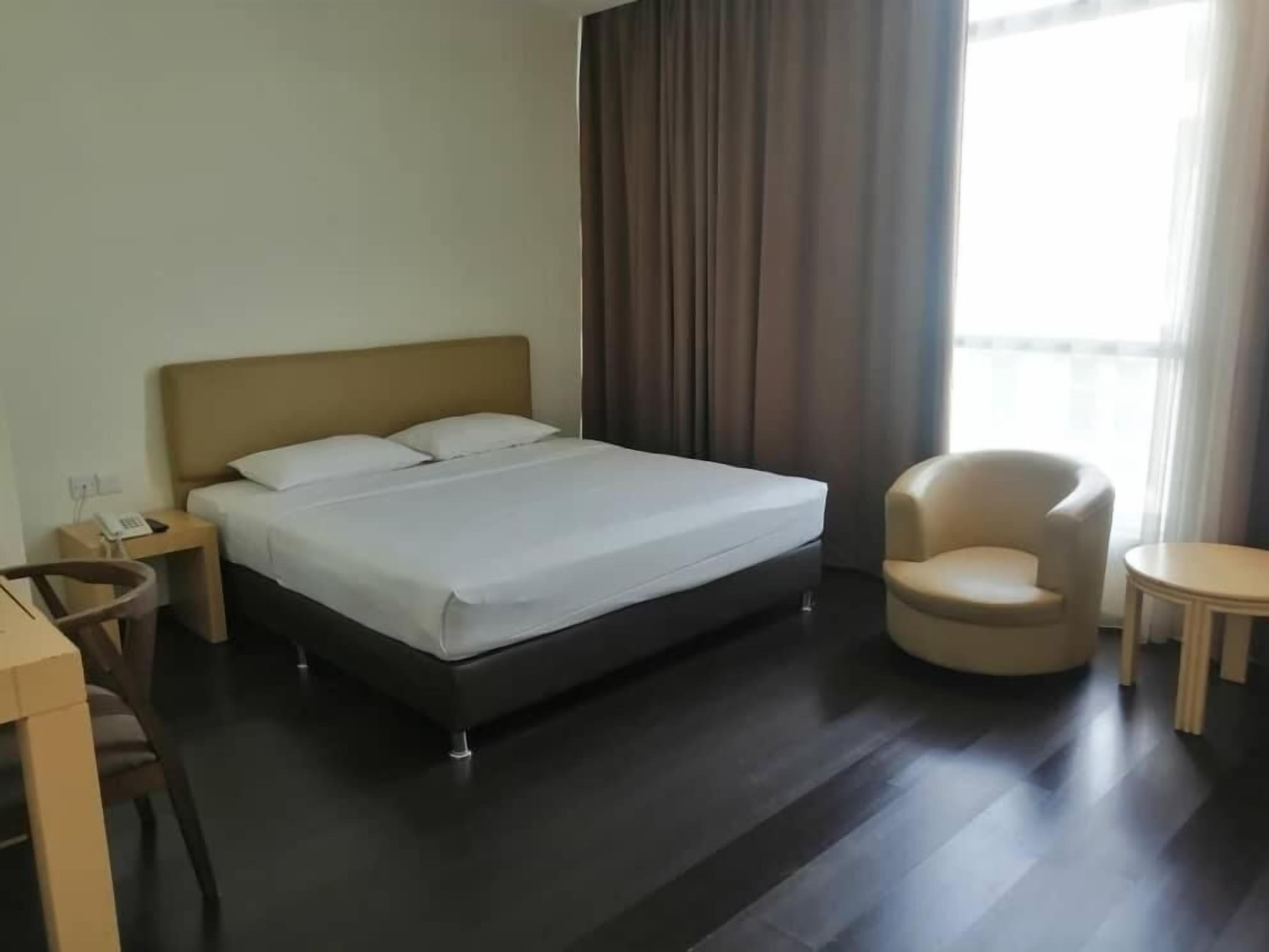 A hotel room with a bed, a chair, a small table, and a nightstand with a phone.