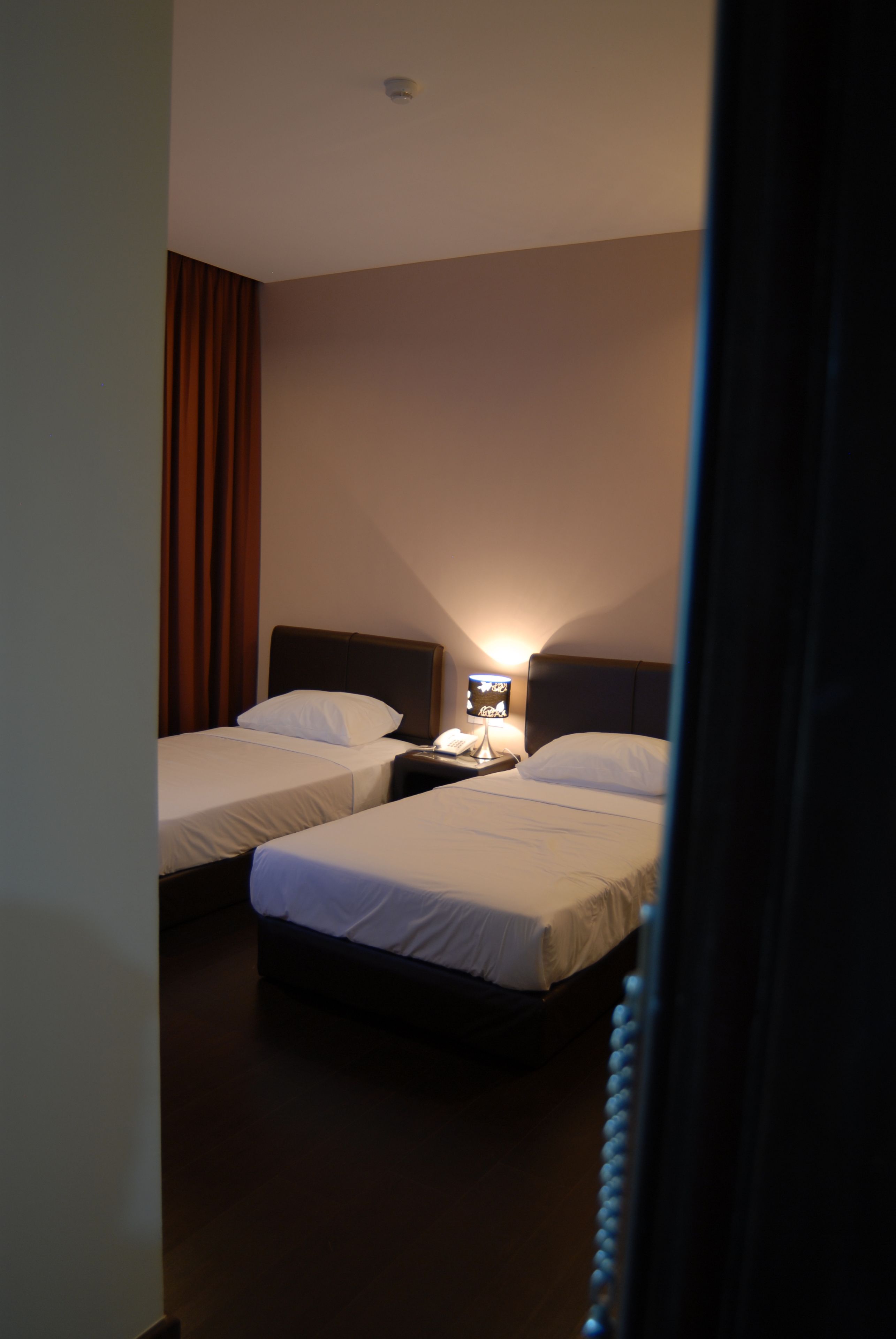 A hotel room with two beds, a nightstand, a lamp, and a television.