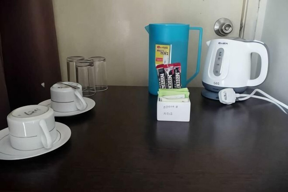 A kitchen counter with a coffee maker, a blue pitcher, a box of coffee pods, and a set of white cups and saucers.