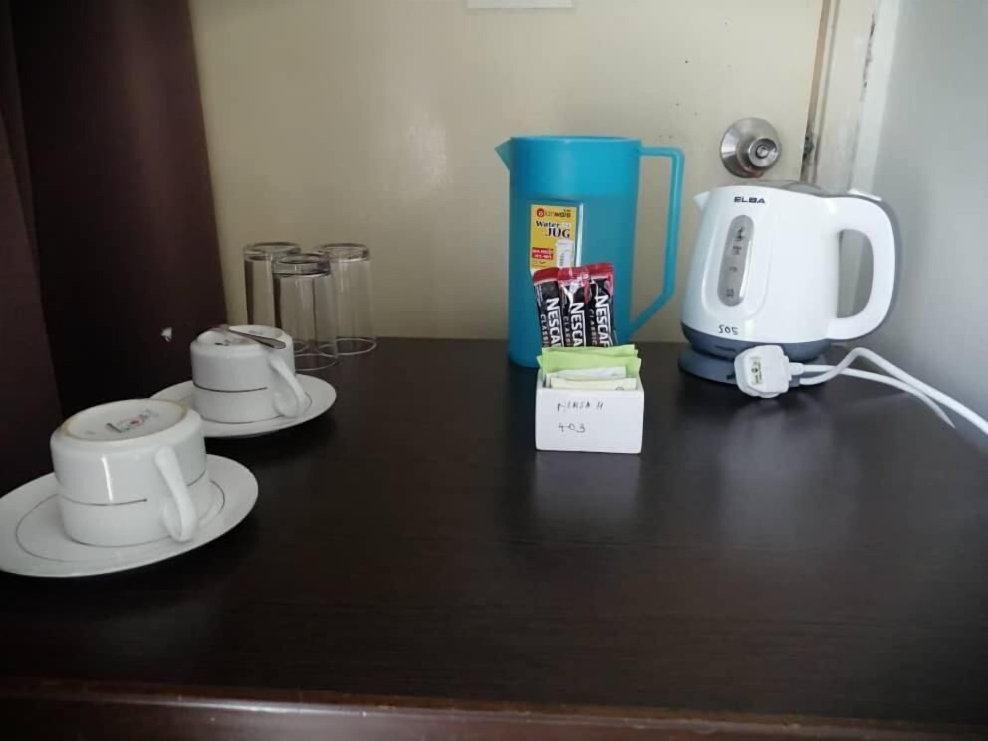 Una mesa con cafetera, jarra de agua, tazas y una caja etiquetada 'Nescafe'.