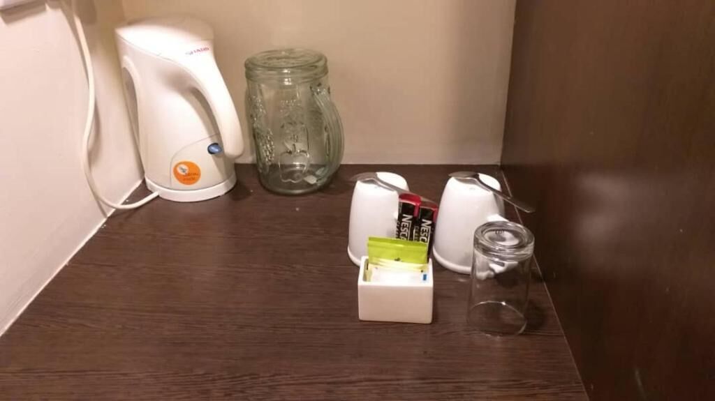 Una encimera de cocina con una cafetera, un tarro de vidrio y una caja de bolsitas de té.