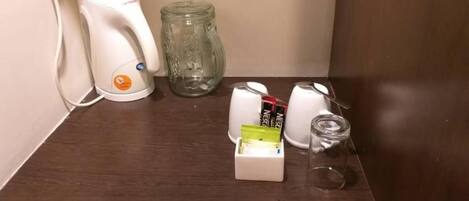 Una encimera de cocina con una cafetera, un tarro de vidrio y una caja de bolsitas de té.