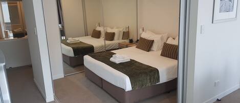 A hotel room with two beds, a large mirror, and a small bedside table.