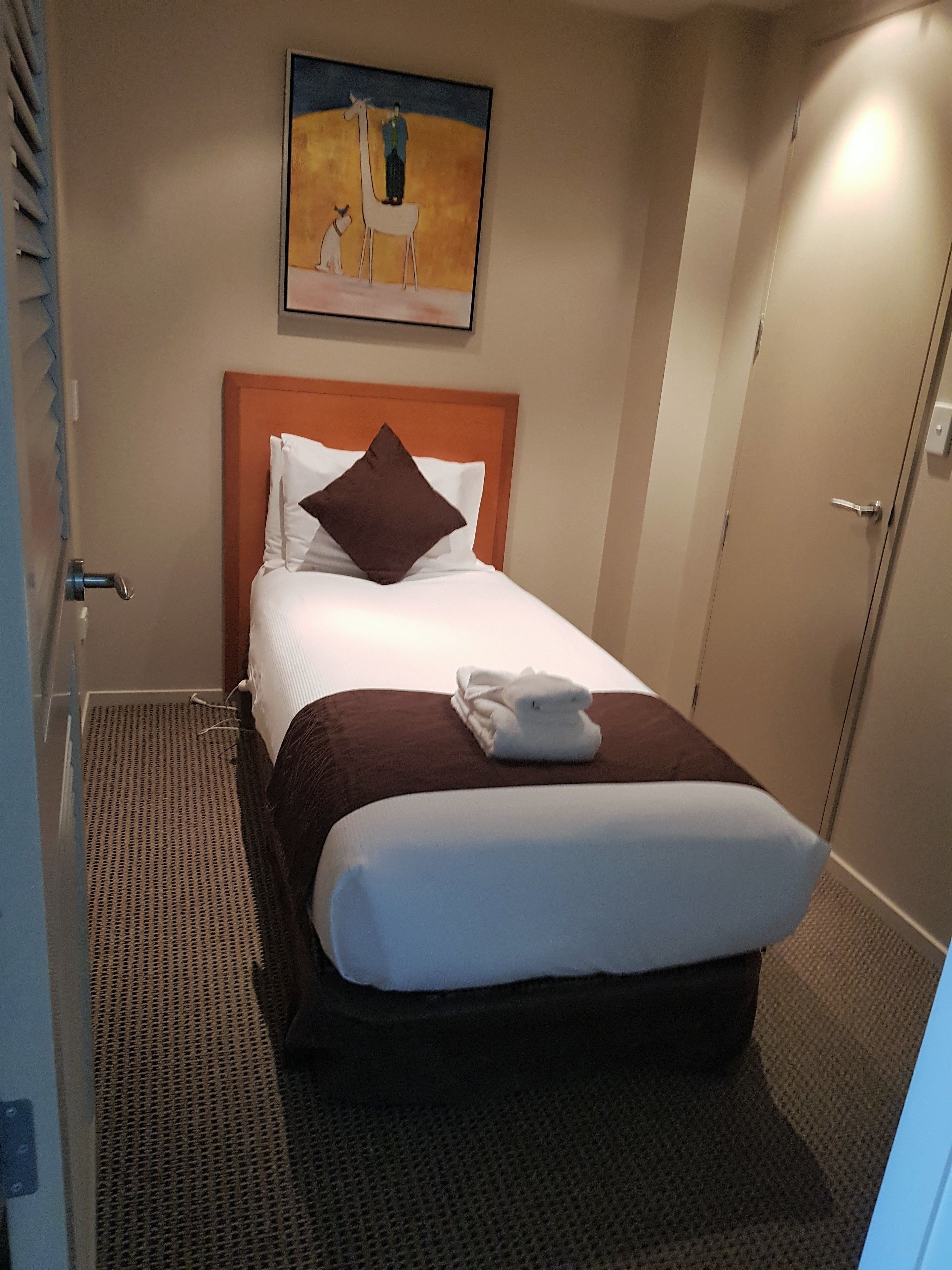 Una camera d'hotel con un letto, un quadro appeso al muro e una porta.