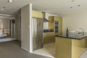 A modern kitchen with stainless steel appliances, a central island, and a view to a balcony. - Quest on Durham (Tauranga)