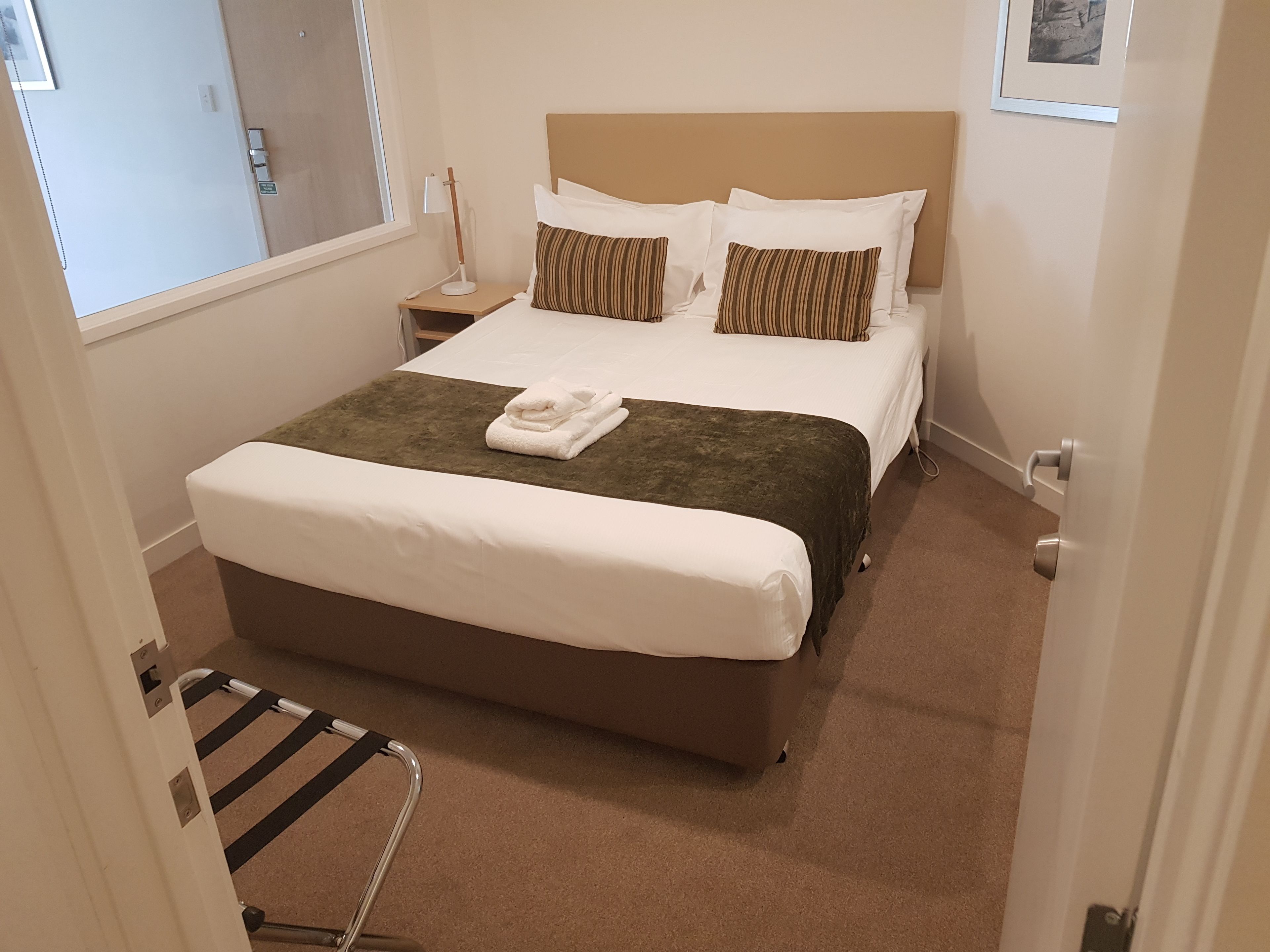 A hotel room with a large bed, a bedside table, a lamp, and a window.