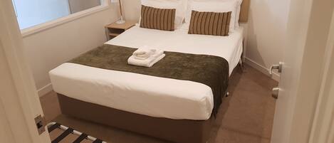 A hotel room with a large bed, a bedside table, a lamp, and a window.