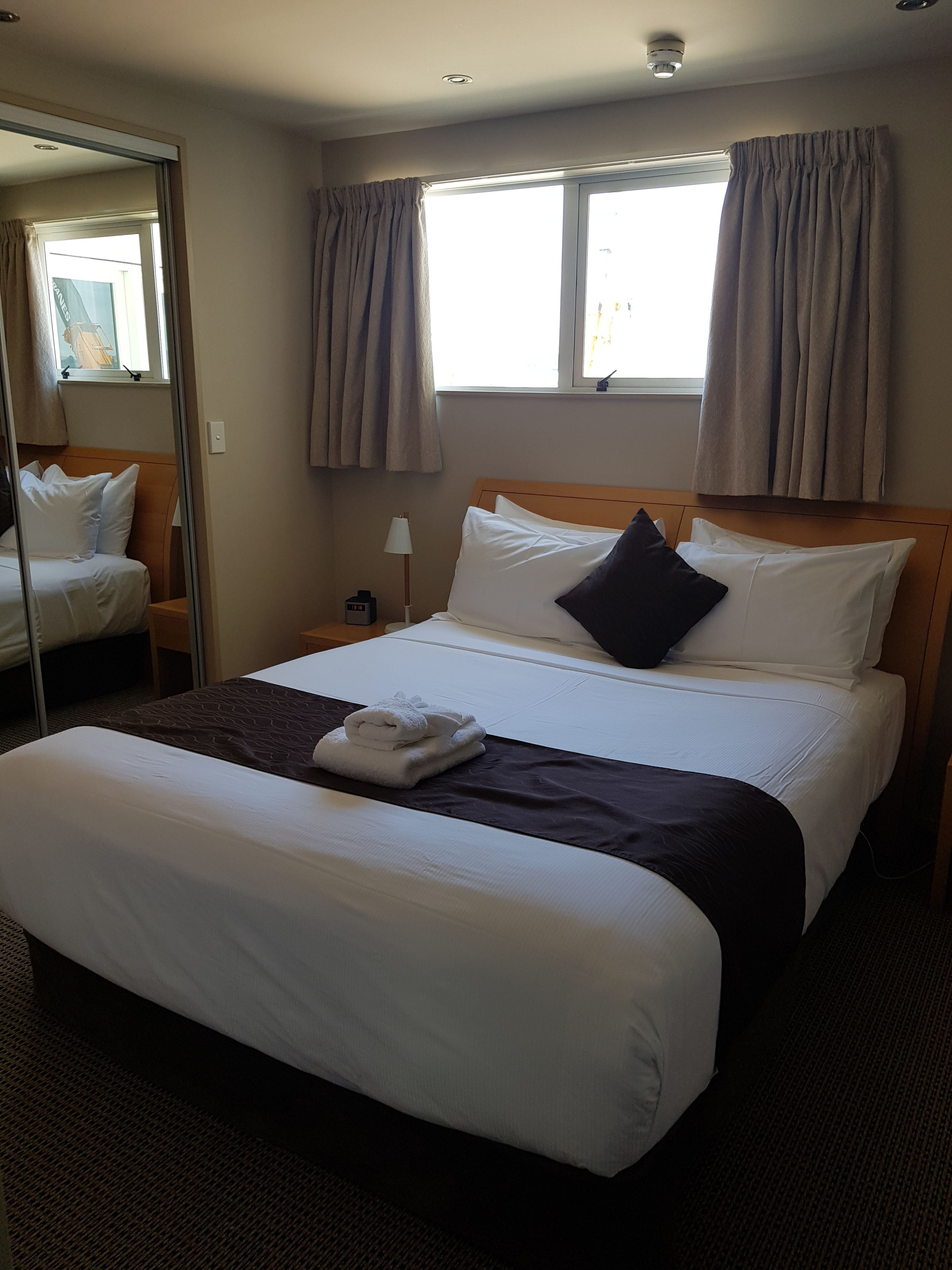 A hotel room with a large bed, a bedside table with a lamp, and a mirror.