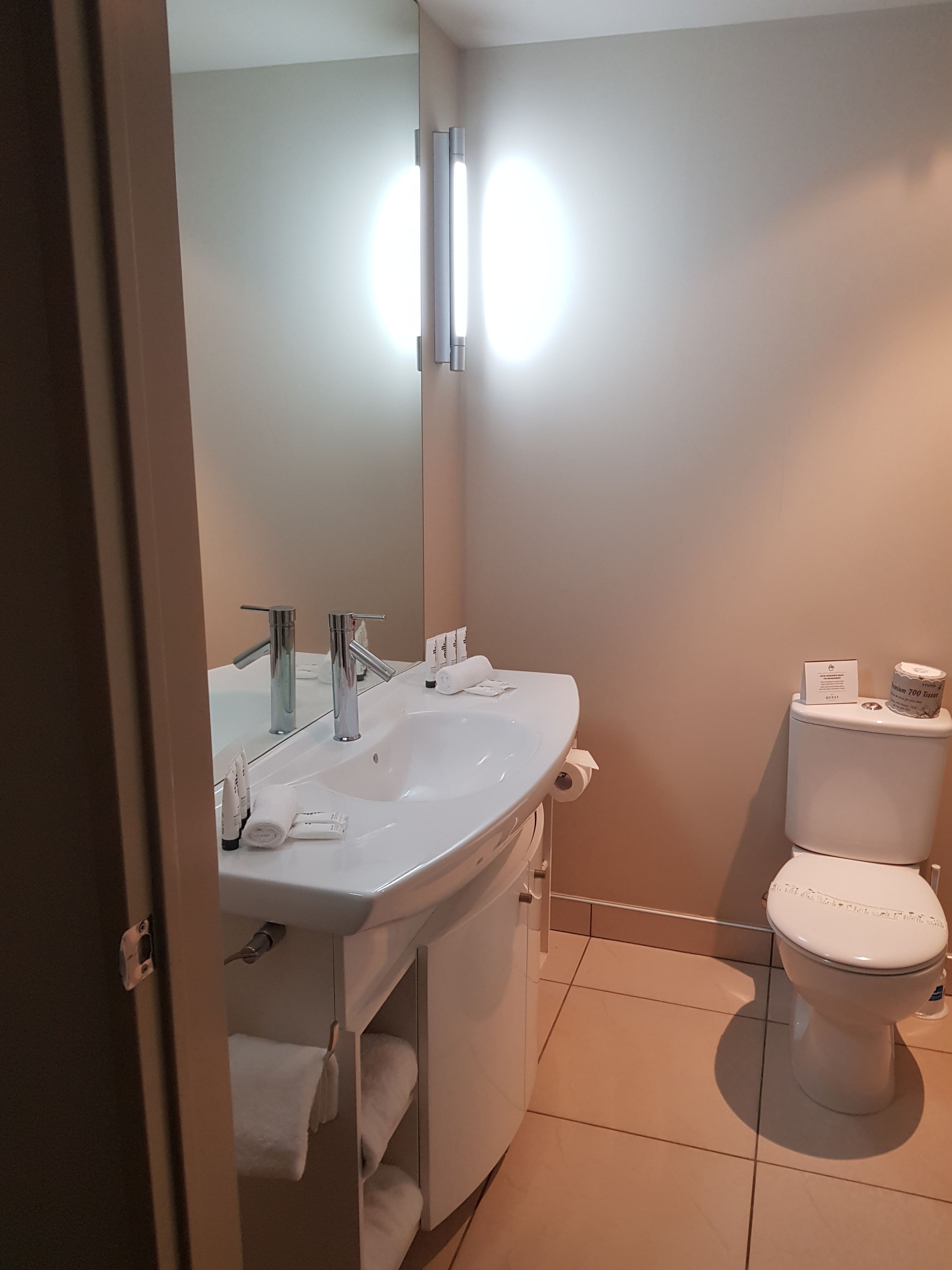 A bathroom with a white sink, mirror, and toilet.