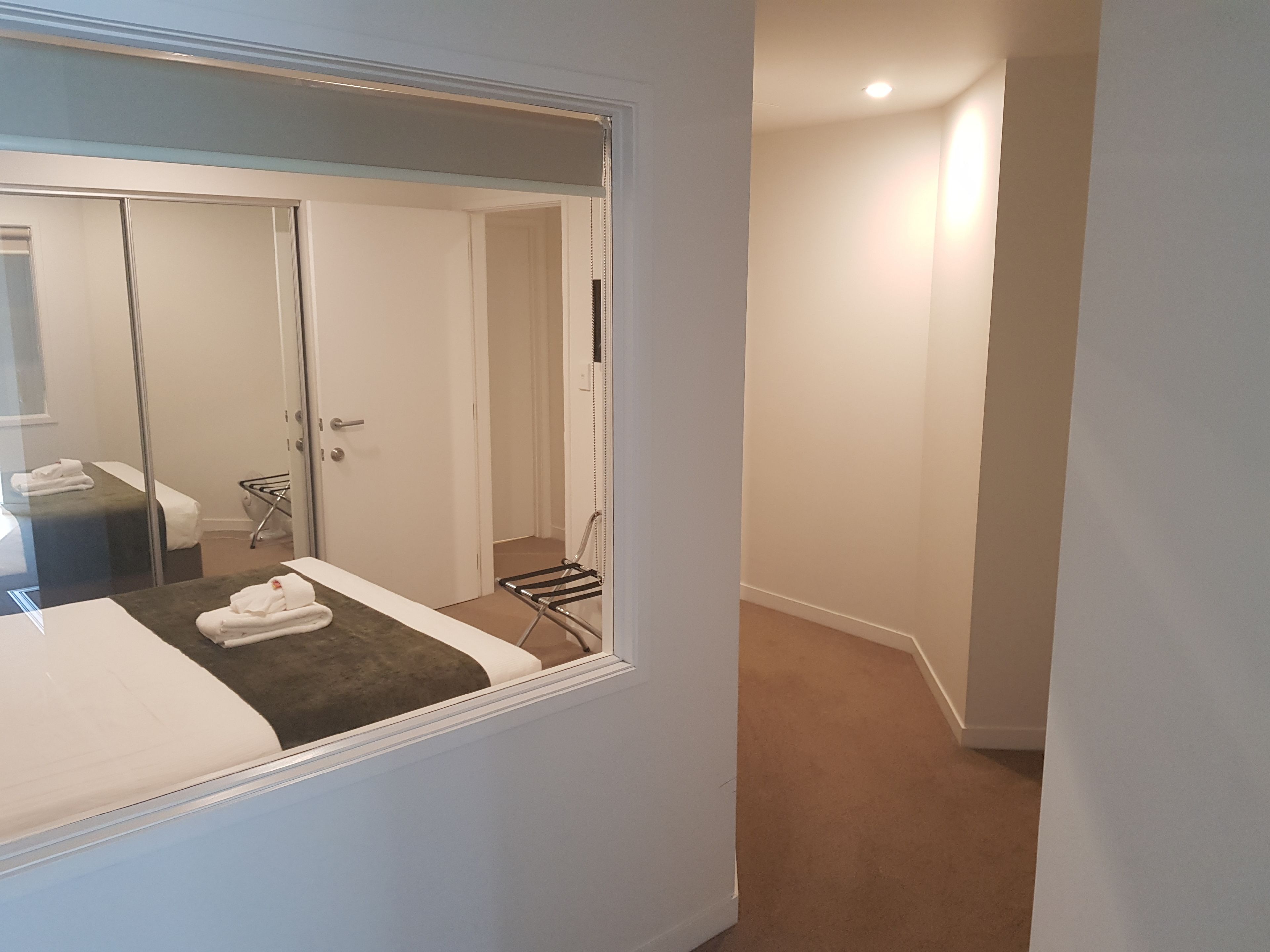 A hotel room with a large mirror, a bed, a towel rack, and a door leading to a hallway.