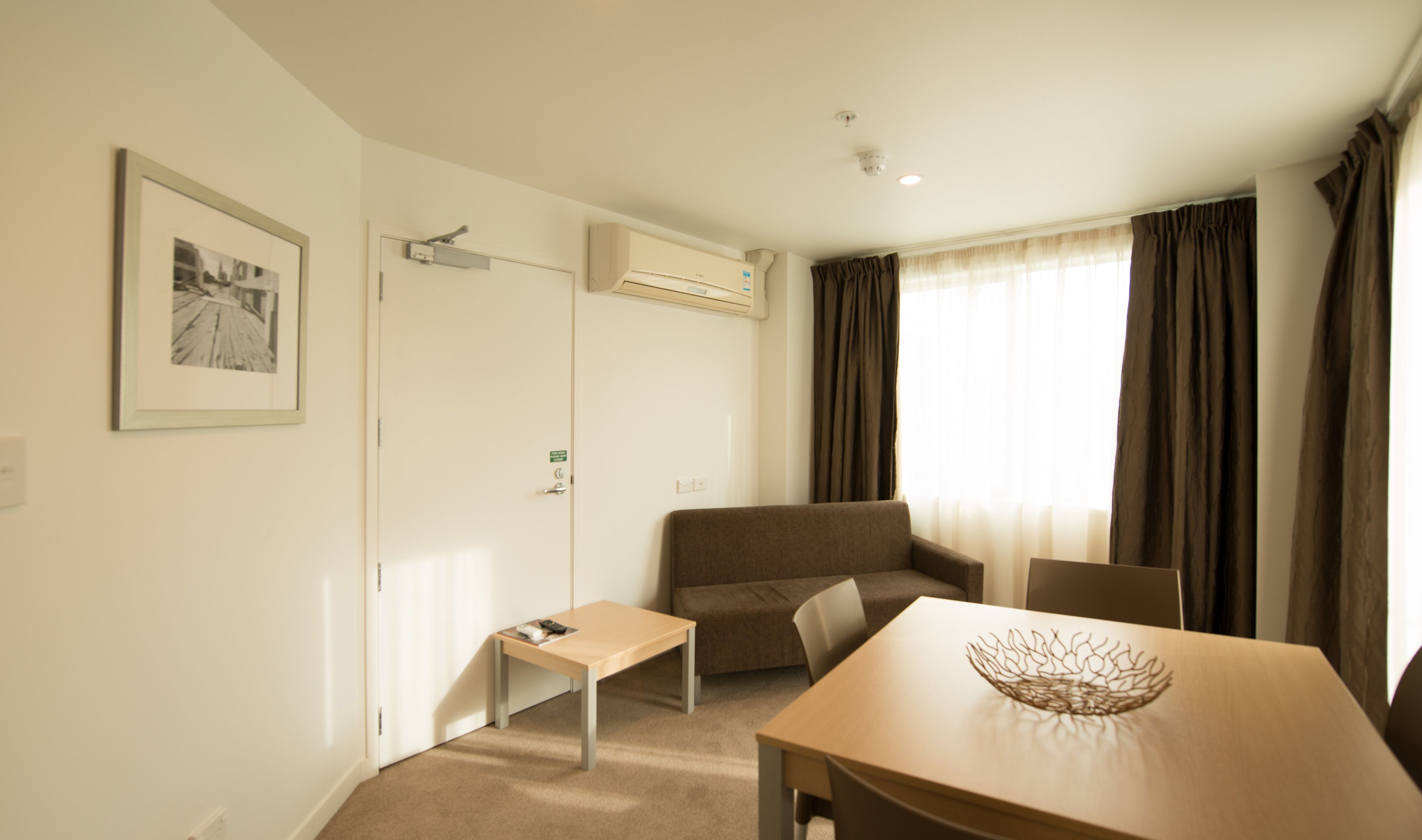 A hotel room with a sofa, a small table, a chair, and a decorative bowl on the table.