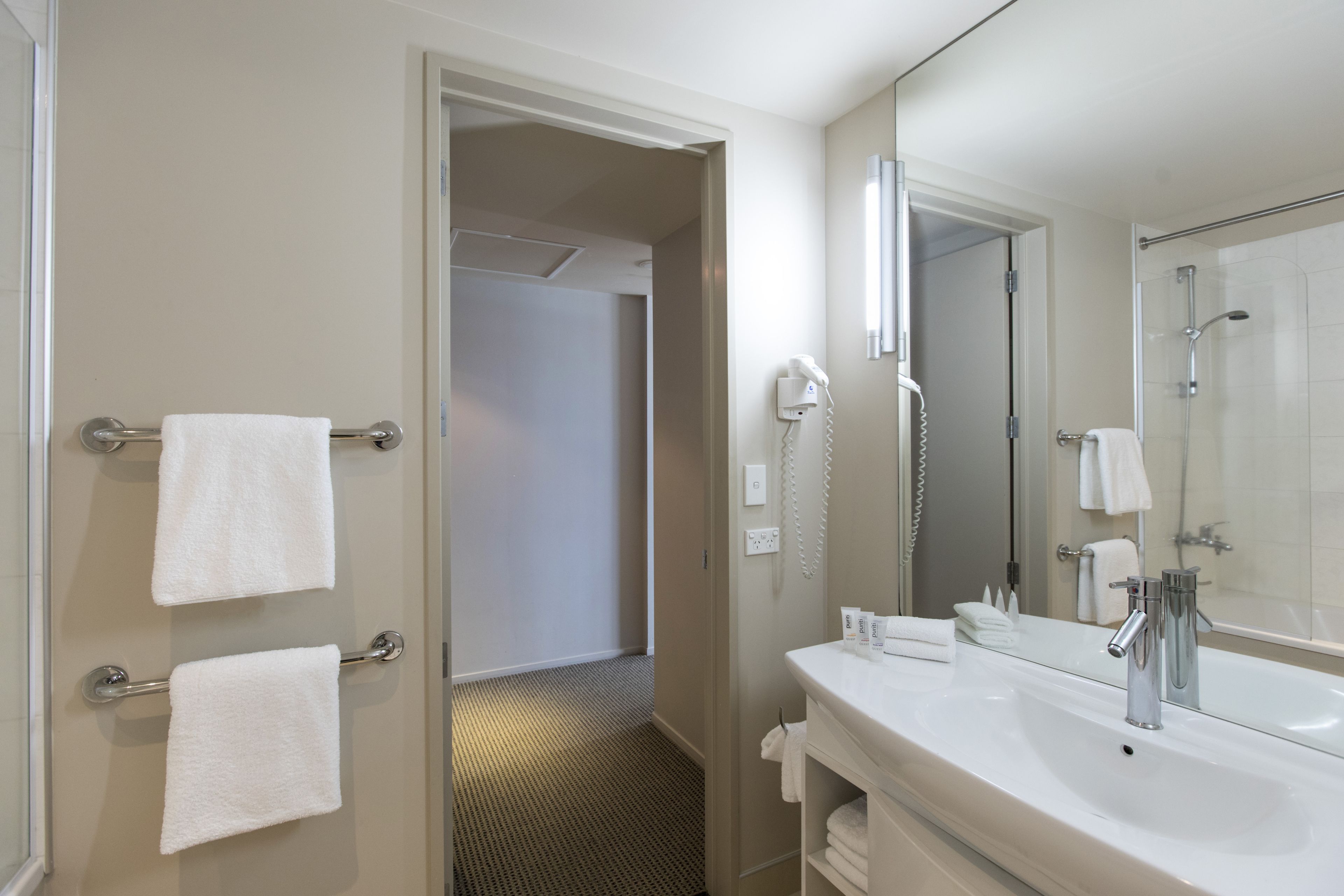 A hotel bathroom with a large mirror, a sink, and a shower area.