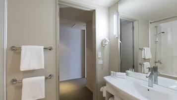 A hotel bathroom with a large mirror, a sink, and a shower area.