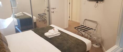 A hotel room with a bed, a TV mounted on the wall, and a small table with a towel and a fan.