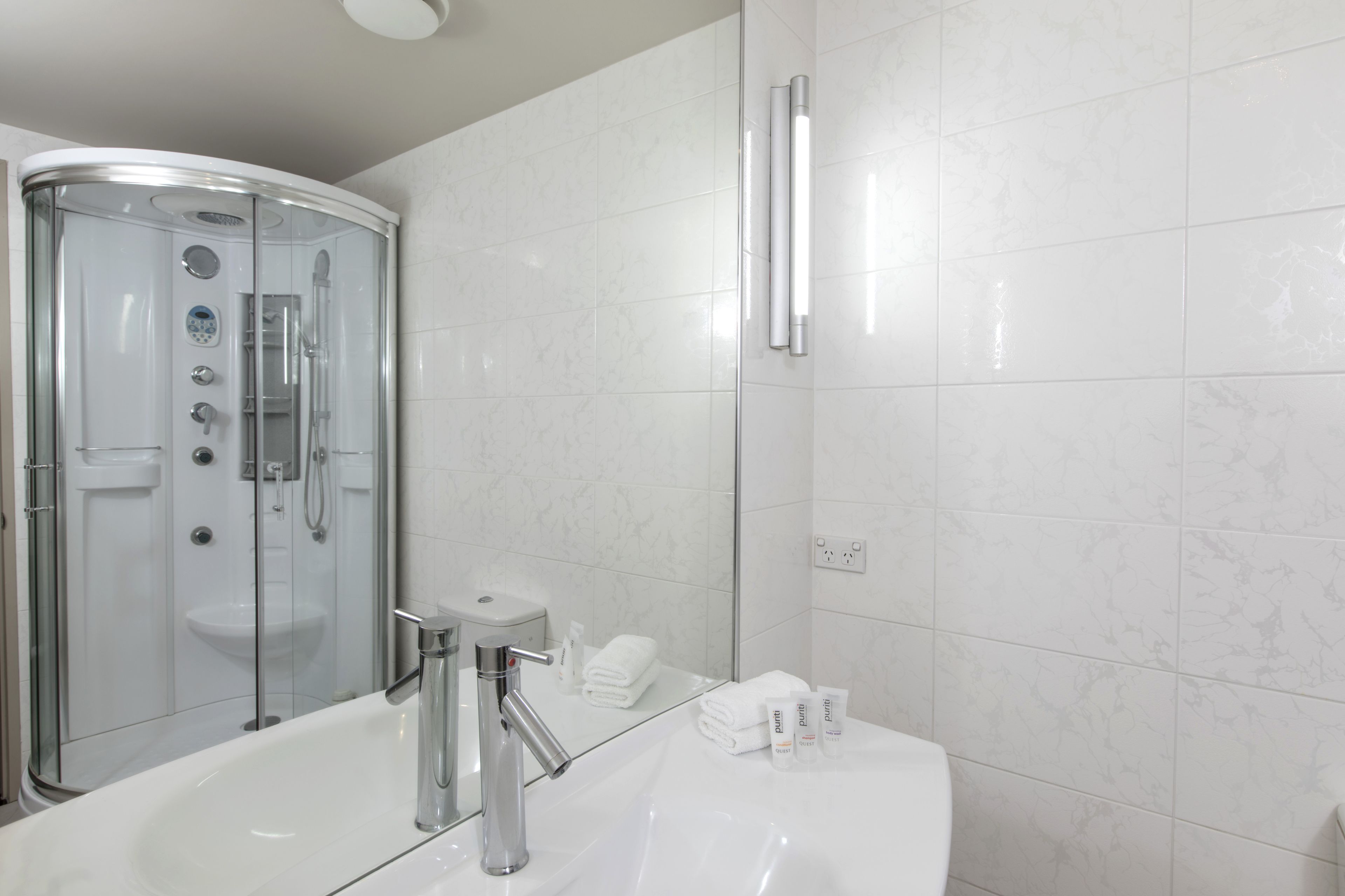 A modern bathroom with a glass-enclosed shower, a white sink, and a mirror.