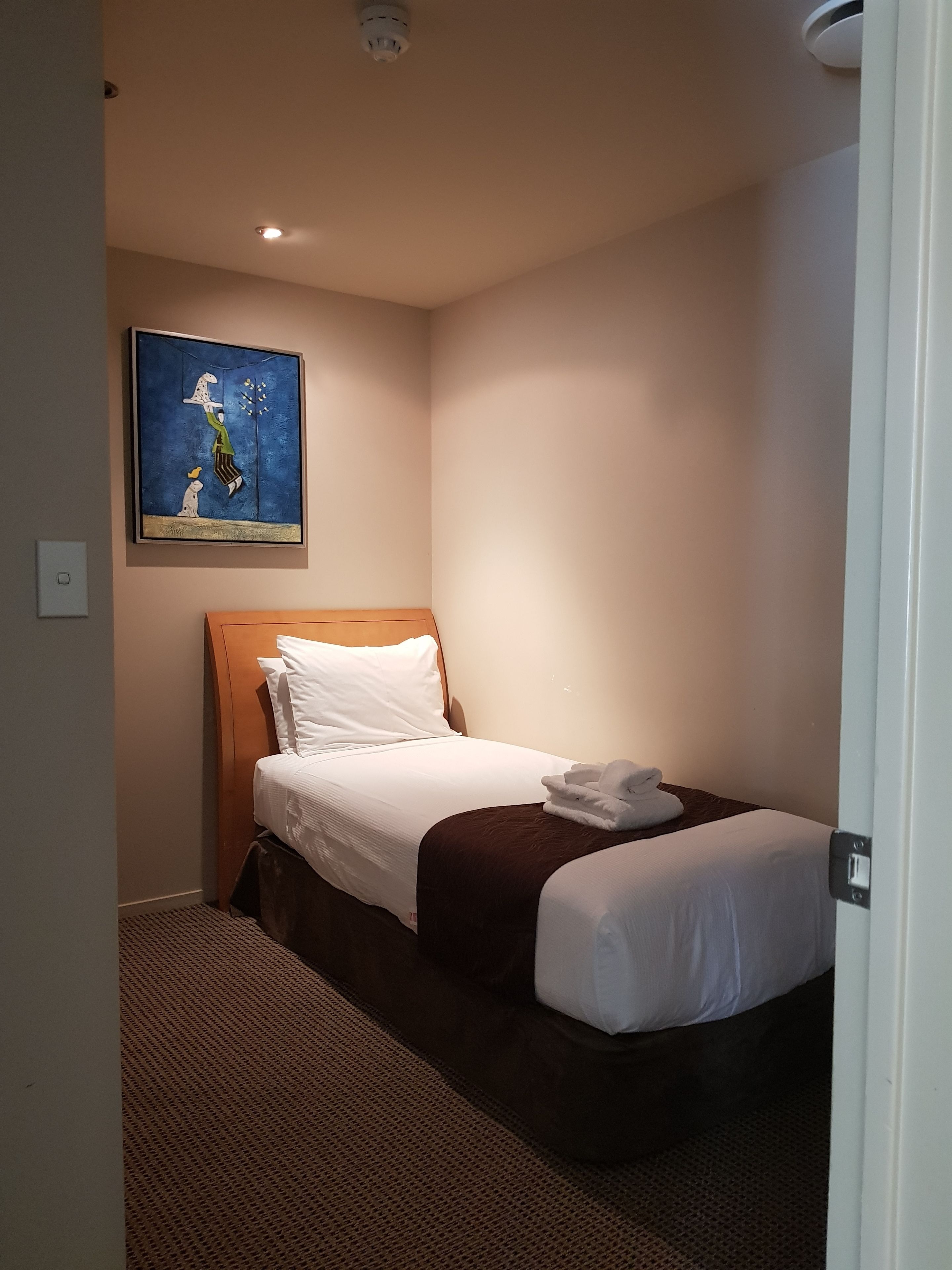 A hotel room with a bed, a painting on the wall, and a door.