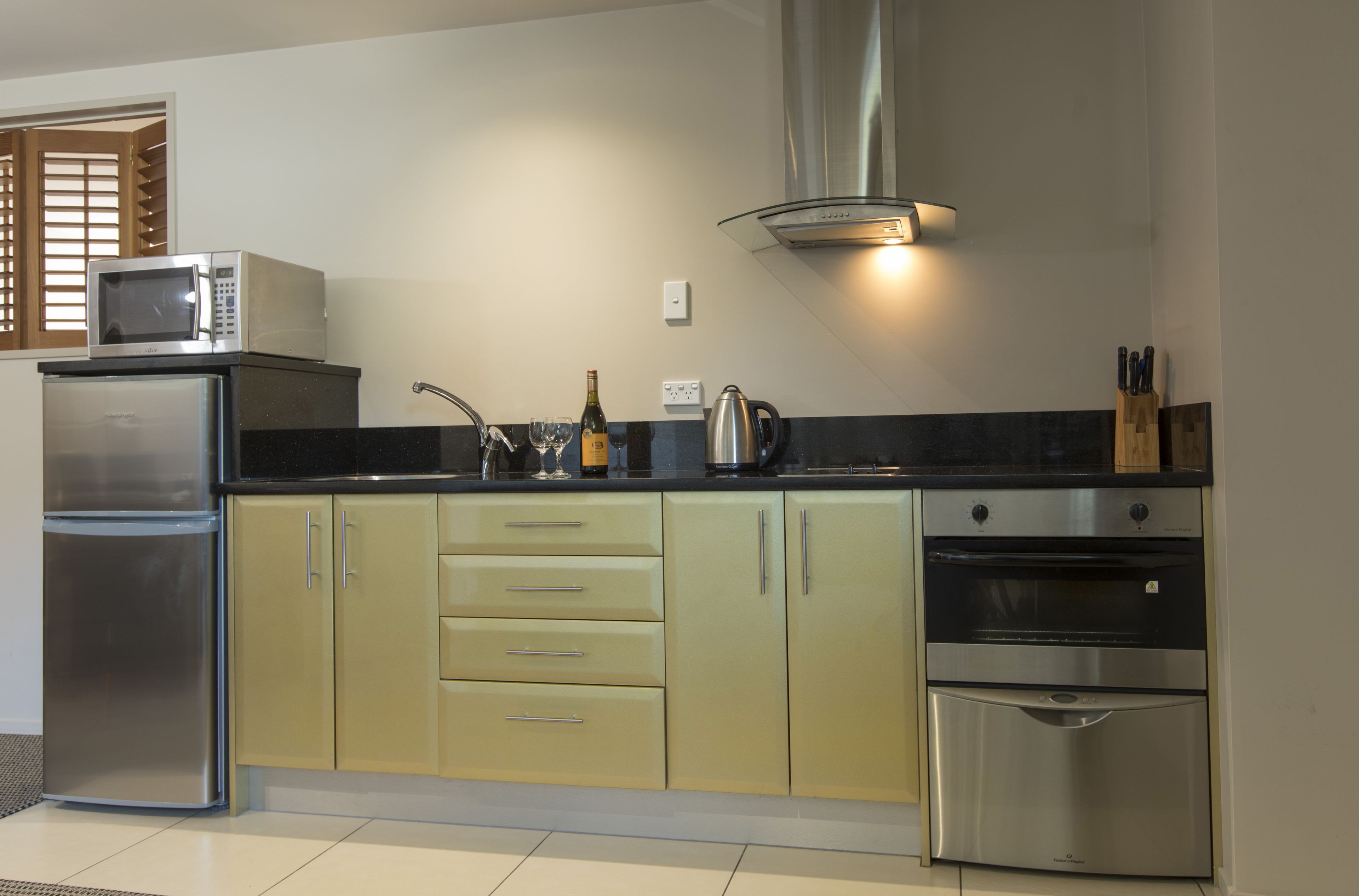 Una cocina equipada con microondas, refrigerador, horno y una botella de vino.