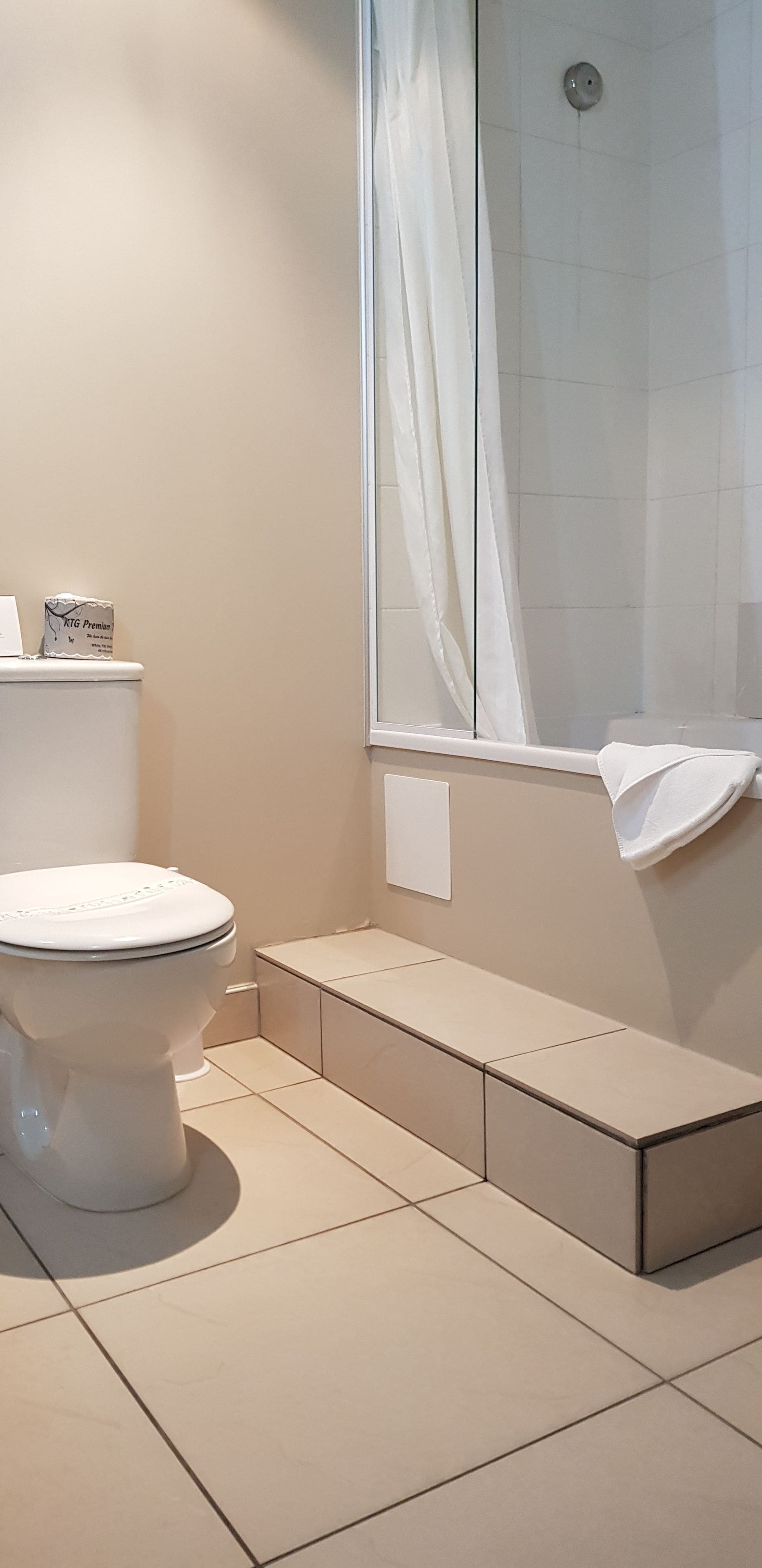 Une salle de bain moderne avec des toilettes, un espace douche doté d’une porte en verre, et une serviette accrochée au mur.