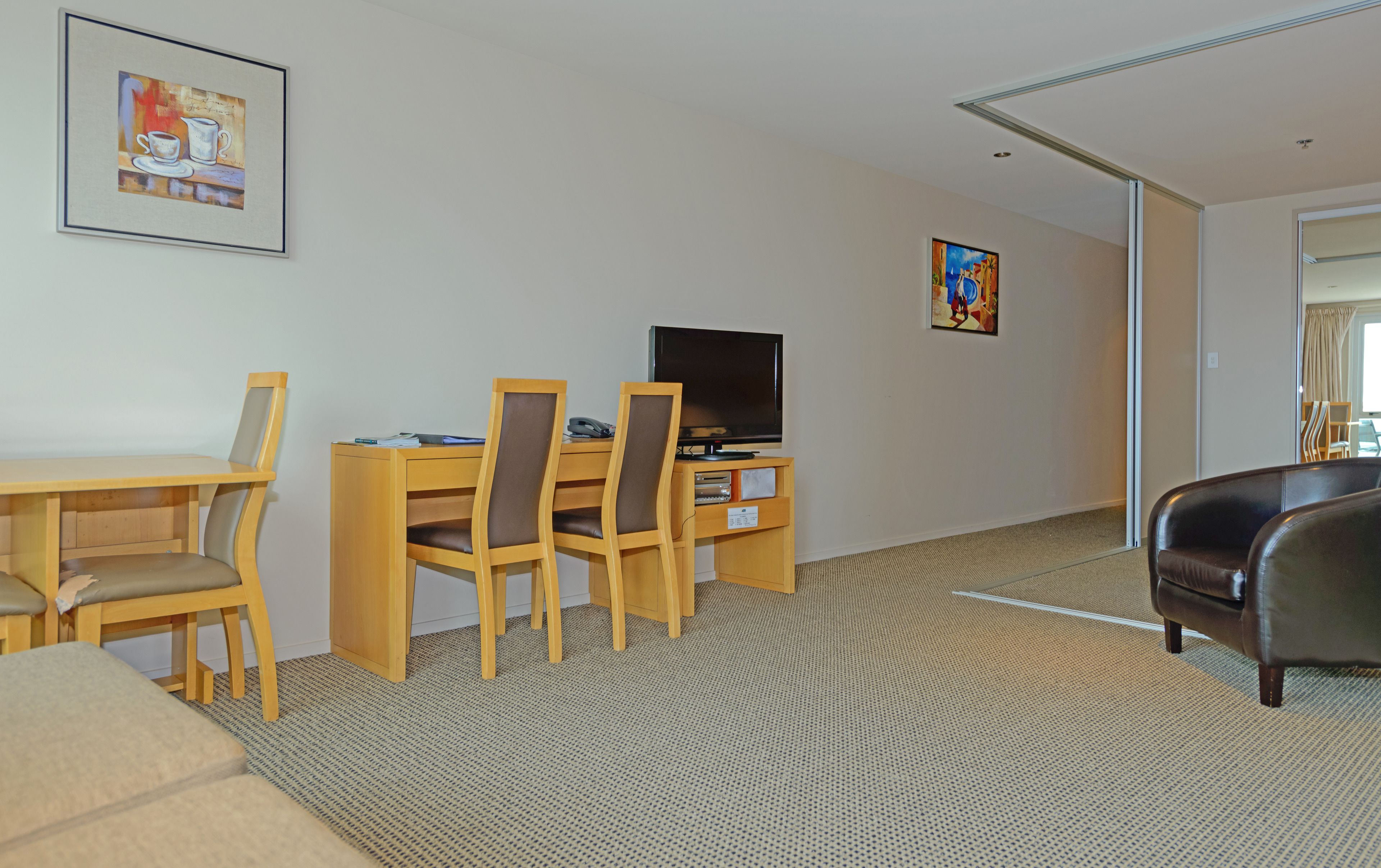 A hotel room with a wooden desk, two chairs, a television, and a sofa.